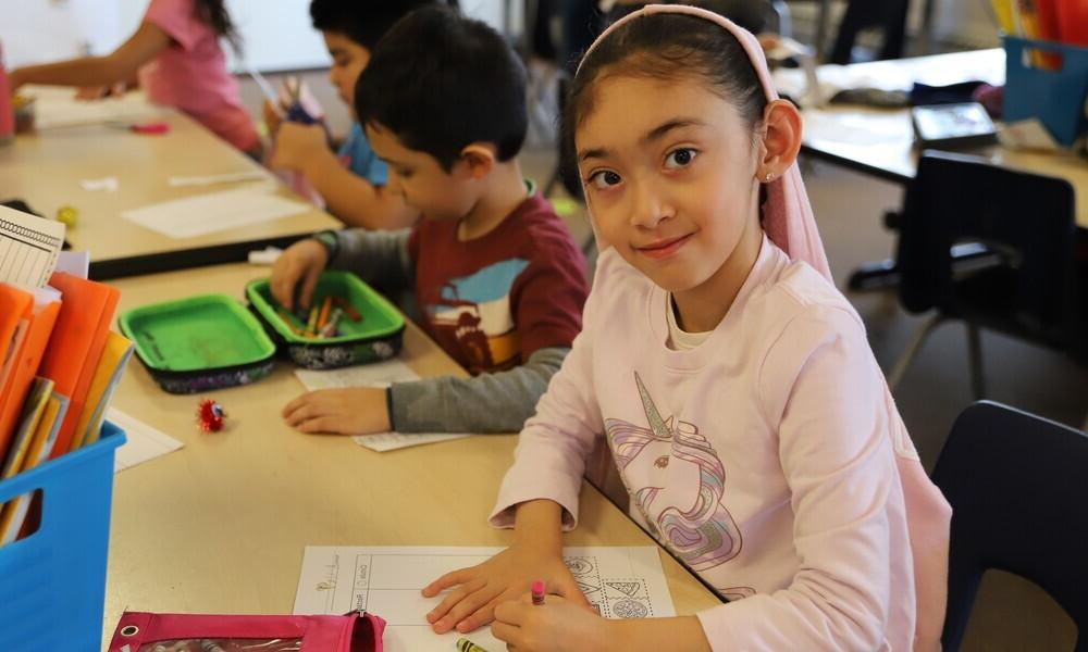 Young girl with pink unicorn shirt coloring at school